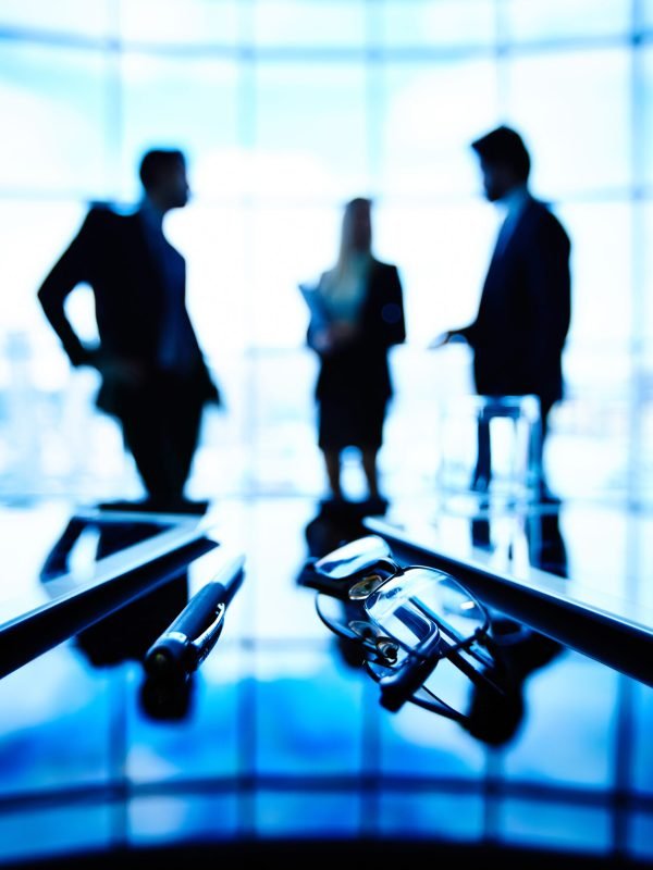 Office life Image of eyeglasses, touchpads and pen at workplace with group of businesspeople communicating on the background